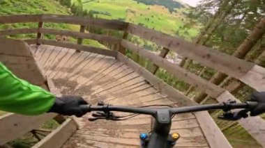 Dağ bisikletçisi orman bisiklet yolu boyunca eğri bir tahta kaldırımdan iniyor. Bisiklet parklarında engebeli patikalarda sürerken teknik beceriler ve heyecan. Adrenalin doğadaki açık hava maceraları
