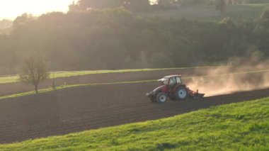 Çiftçi tarlayı kış uykusuna ve bahar mevsiminde ekime hazırlıyor. Traktör hareket ederken, altın sabah ışığında tarla sürerken havada toz yükselir..