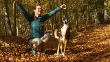 Neşeli kahverengi köpek, gülen sahibi düşen sonbahar yapraklarını havaya fırlattığında zıplar. Deniz mavisi ceketli genç bir kadın köpeğinin yanında diz çöker ve ormanda yürürken renkli yapraklarla oynarlar.