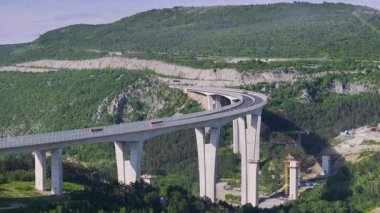 Slovenya 'nın kırsal kesimlerinde güneşli bir yaz gününde yoğun Crni Kal viyadükünün manzaralı uçuşu. Slovenya 'nın dağlık karst manzarasını geçen modern otoyol köprüsünün üzerinde uçuyor.