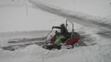 Şiddetli bir kar fırtınası sırasında buzla kaplı bir yolu temizleyen adam. Fırıl fırıl dönen kar taneleri ve buzlu hava, ağır akıntıları yaran saban gibi enerjik bir kış ayarı oluşturur..