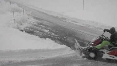 Yol ayrımındaki yoğun bir yolda kar küreyen bir adam. Etrafı kar fırtınasıyla çevrili. Rüzgârlar, kar tanelerini her yöne savurarak sahneyi sürekli değişen bir kış manzarasına dönüştürüyor..