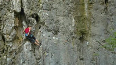 Açık havada dik, dokulu kireçtaşı bir duvara tırmanan tanınmayan bir kadın. Sakin doğada dik bir duvara tırmanan atletik bir kadının aksiyon sahnesi. Sıra dışı tırmanış.