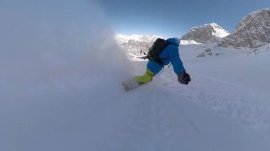 Dağlarda açık bir kış gününde kar taneleri üzerinde süzülen snowboardcu. Mükemmel koşullar ve nefes kesici dağ manzaraları, dağlık bölgede snowboard yapmanın saf neşesini vurguluyor..