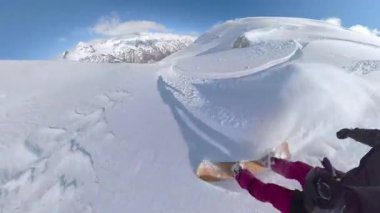 Yüksek dağlarda güneşli bir günün tadını çıkaran snowboardcu derin, el değmemiş karda ustaca oyup zarafetle dönüyor. Karlı Arnavut Alplerinde resim gibi snowboard macerası.