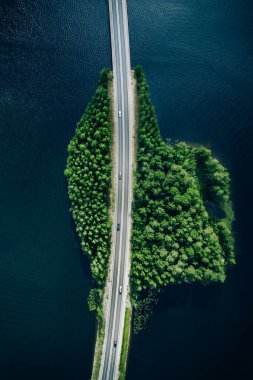 Aerial view of road through blue lakes or sea with green summer woods in Finland.