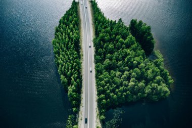 Aerial view of road through blue lakes or sea with green summer woods in Finland.