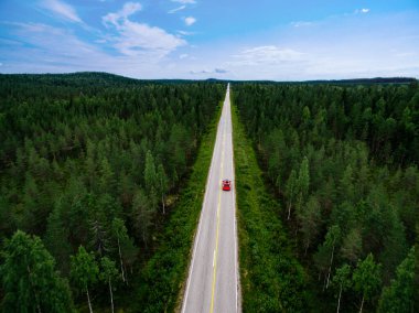 Aerial view of red car with roof rack driving the route through green summer woods in Finland.