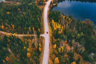 Aerial view of road with car through fall woods with green and yellow trees in Finland. Beautiful autumn landscape.