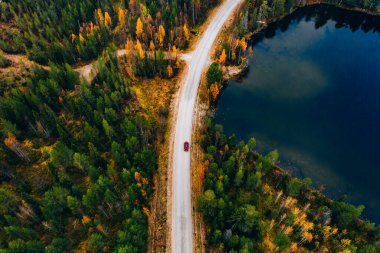 Aerial view of road with car through fall woods with green and yellow trees in Finland. Beautiful autumn landscape.