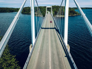 Aerial view of modern suspension bridge with car or truck over the blue lake water in summer Finland