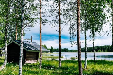 Finnish wood-fired log sauna by blue lake on summer day in Finland