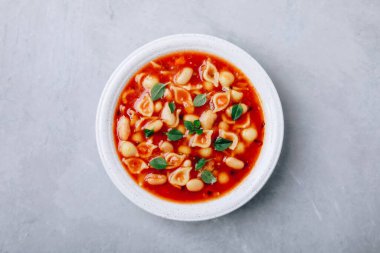 Tomato soup. Minestrone soup. Tomato bean and pasta soup bowl on gray stone background. Top view, copy space.
