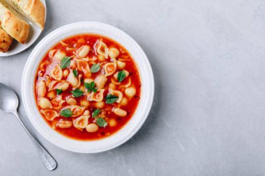 Tomato soup. Minestrone soup. Tomato bean and pasta soup bowl with toasts on gray stone background. Top view, copy space.