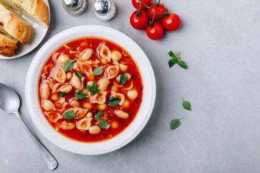 Tomato soup. Minestrone soup. Tomato bean and pasta soup bowl with toasts on gray stone background. Top view, copy space.