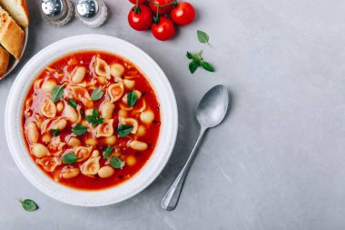 Tomato soup. Minestrone soup. Tomato bean and pasta soup bowl with toasts on gray stone background. Top view, copy space.