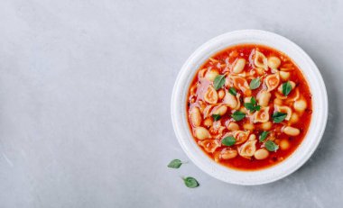 Tomato soup. Minestrone soup. Tomato bean and pasta soup bowl on gray stone background. Top view, copy space.