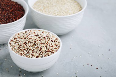 Quinoa. Red white brown quinoa seeds in bowl. Mixed organic raw quinoa seeds on gray stone background.