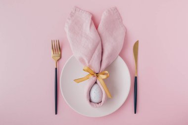 Happy Easter table setting with egg in napkin Easter Bunny and golden cutlery. Top view, copy space.