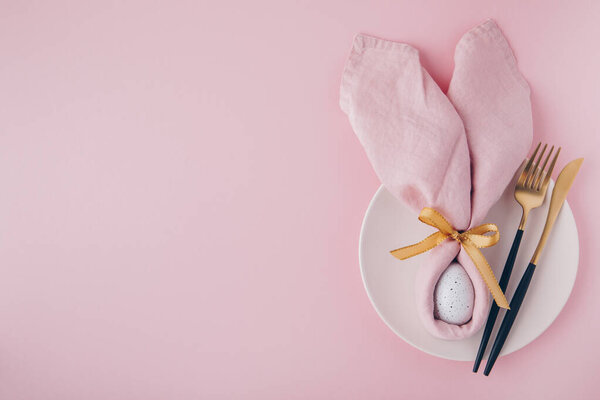 Happy Easter table setting with egg in napkin Easter Bunny and golden cutlery. Top view, copy space.