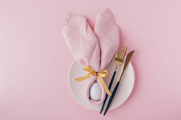 Happy Easter table setting with egg in napkin Easter Bunny and golden cutlery. Top view, copy space.