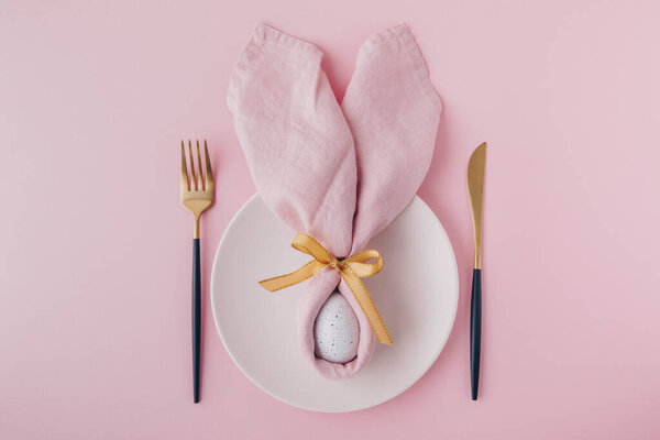 Happy Easter table setting with egg in napkin Easter Bunny and golden cutlery. Top view, copy space.