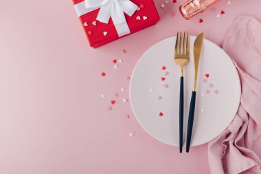Valentine's Day background. A set of golden cutlery and pink napkin on plate with hearts confetti. Top view, copy space.