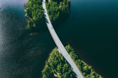 Aerial view of road over blue lake water and green woods in Finland. Beautiful summer landscape.