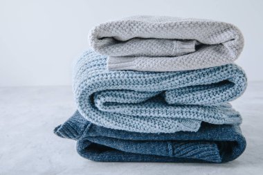 Sweaters. Blue knitted sweaters stacked on gray background.