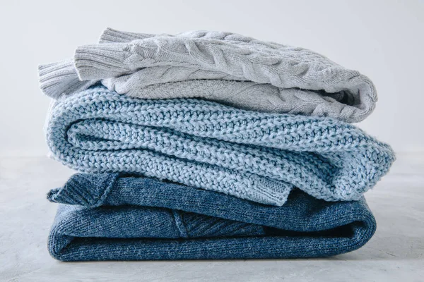 Sweaters. Blue knitted sweaters stacked on gray background.