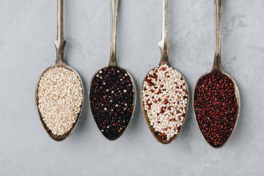 Quinoa. Red black white quinoa seeds in spoon on gray stone background, top view. Set with different types of quinoa in spoons.