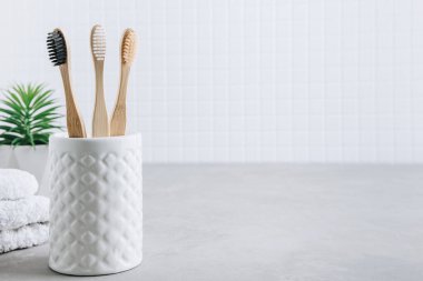 Eko diş fırçaları. Bambu diş fırçaları fincanı, gri taş arka planda beyaz havlular, kopyalama alanı. Asgari banyo arkaplanı