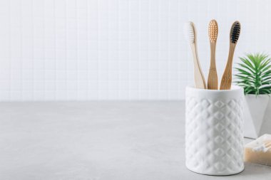 Eko diş fırçaları. Bambu diş fırçası kabı, doğal sabun, plastik ücretsiz kulak çubukları ve gri taş arka planda beyaz havlular, kopyalama alanı. Asgari banyo arkaplanı