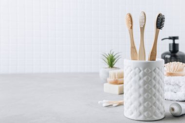Eko diş fırçaları. Bambu diş fırçası fincanı, doğal sabun, plastik ücretsiz kulak çubukları, tahta saç fırçası ve gri taştan arka planda beyaz havlular, kopyalama alanı. Asgari banyo arkaplanı