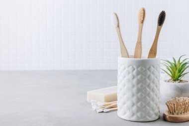 Eko diş fırçaları. Bambu diş fırçası fincanı, doğal sabun, plastik ücretsiz kulak çubukları, tahta saç fırçası ve gri taştan arka planda beyaz havlular, kopyalama alanı. Asgari banyo arkaplanı