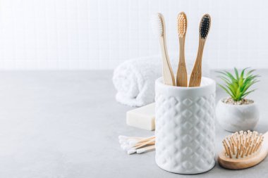 Eko diş fırçaları. Bambu diş fırçası fincanı, doğal sabun, plastik ücretsiz kulak çubukları, tahta saç fırçası ve gri taştan arka planda beyaz havlular, kopyalama alanı. Asgari banyo arkaplanı