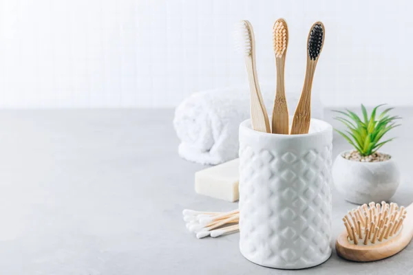 stock image Eco toothbrushes. Bamboo toothbrushes cup, natural soap, plastic free ear sticks, wooden hair brush and white towels on gray stone background, copy space. Minimal bath background