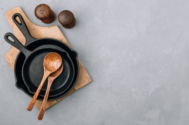 Boş tavalar. Demir tavalar, tahta kaşıklar, gri taş arka plan, üst manzara, kopyalama alanı. Mutfak gereçleri arka plan kavramı.