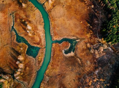 Turkuaz kıvrımlı nehir ve altın rengi sonbahar manzarası.