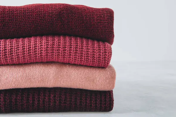 Sweaters. Red, pink sweaters stacked on gray background.