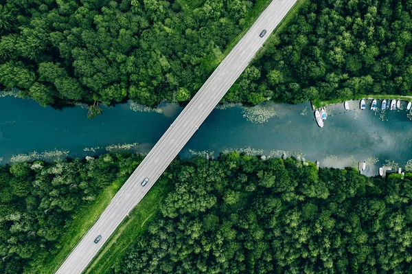 フィンランドの青い川と緑の夏の森の上に車を持つブリッジロードの空中ビュー ストックフォト