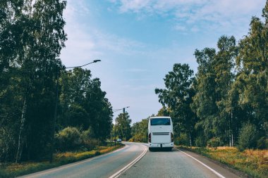 Finlandiya 'nın kırsal kesiminde sonbahar ile yaz ormanı arasında asfalt yolda giden beyaz otobüs.