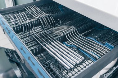 Bulaşıkçı. Temiz aletlerle bulaşık makinesini aç. Temiz paslanmaz çatal, bıçak, kaşık ve çatal takımı olan bulaşık makinesini açın. Çatal bıçaklı bulaşık makinesinin içinde..