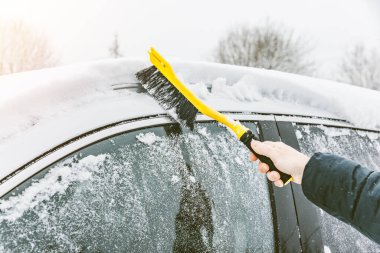 Man cleaning car from snow with yellow brush in winter time. Removing snow from car windows. clipart