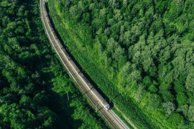 Güzel yeşil yaz ormanlarında trenin insansız hava aracı görüntüsü. Tren istasyonuna giden uzun banliyö treni.