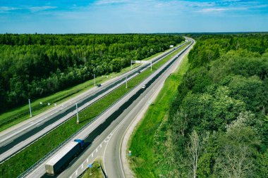 Otoyol asfalt yolunun yeşil yaz ormanlarından geçen araba ve kamyonlarla hava aracı görüntüsü..