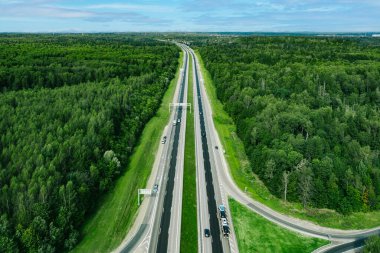 Otoyol asfalt yolunun yeşil yaz ormanlarından geçen araba ve kamyonlarla hava aracı görüntüsü..