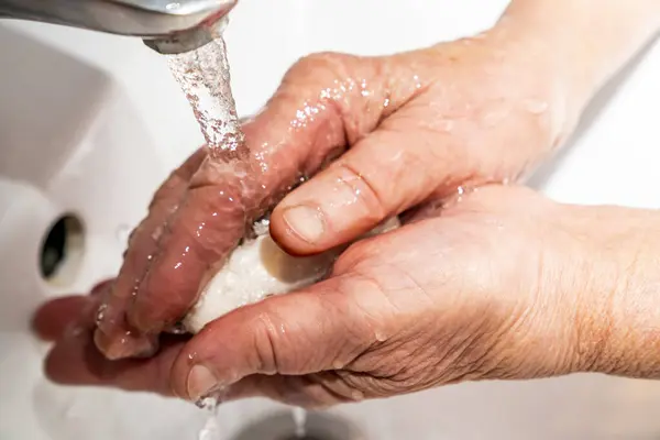 An elderly man washes his hands with soap, wrinkles, old.