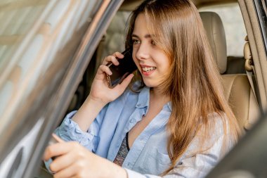 Genç ve güzel bir kız arabada telefonla konuşuyor. 