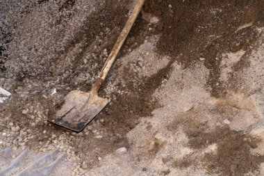 İnşaat kumunun üzerinde duran eski metal kürek. Kumlu dokuda yıpranmış saplı bir kürek resmi. İnşaat ve inşaat alanı kavramı.